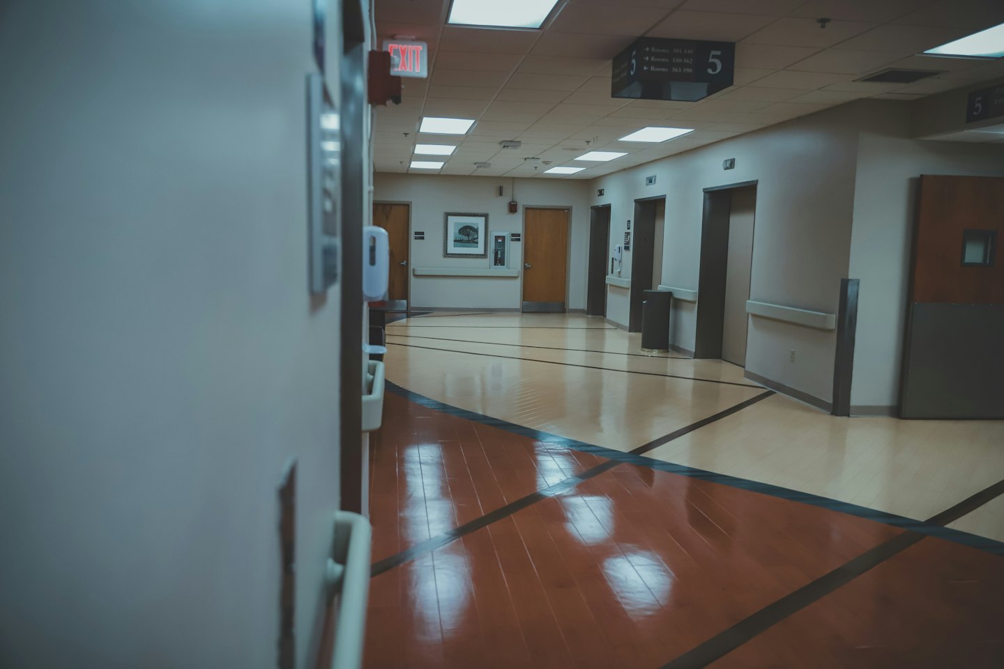 Pasillo de hospital vacío con puertas de madera y ascensores plateados.